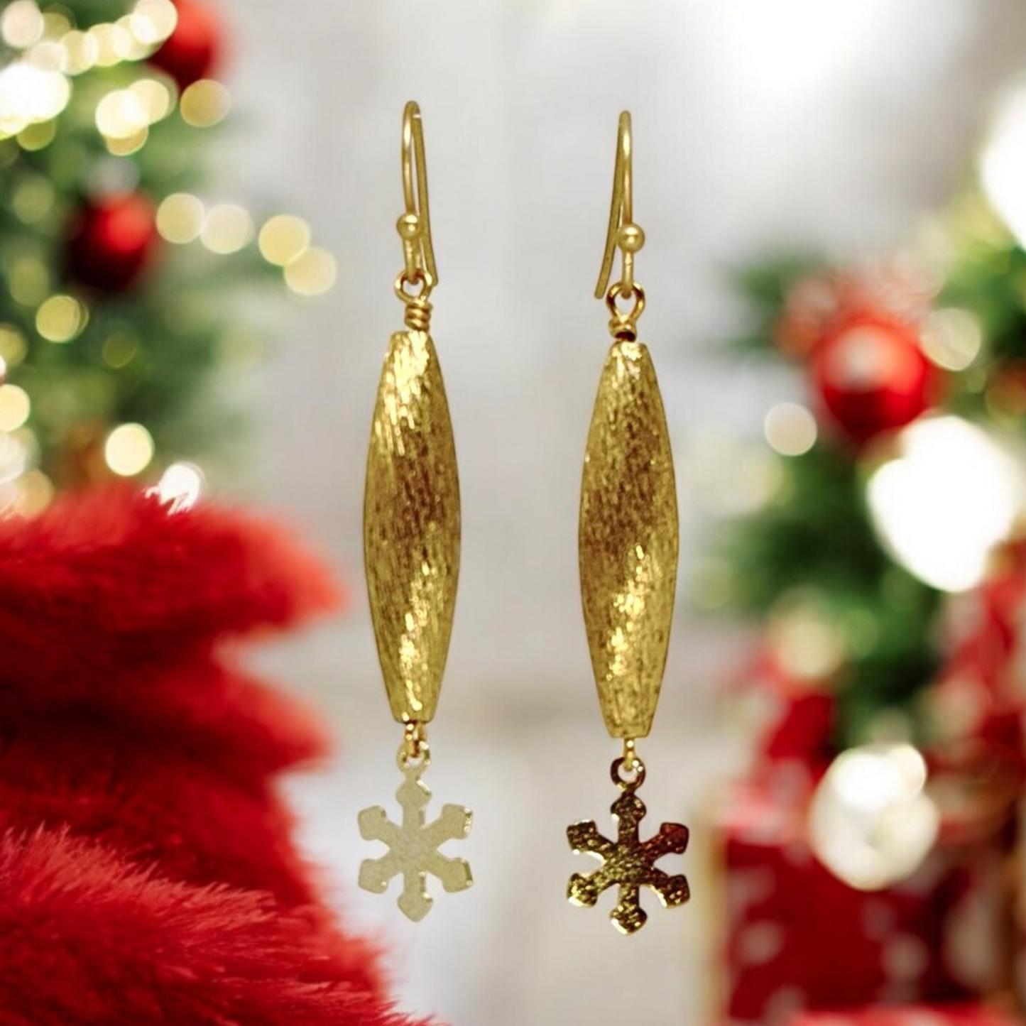 Close-up view of gold textured pod earrings with a small snowflake charm dangling below, showcasing their delicate and minimalist design.