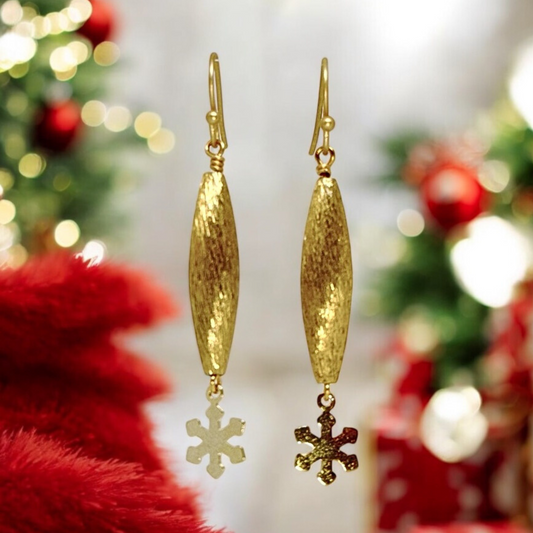 Close-up view of gold textured pod earrings with a small snowflake charm dangling below, showcasing their delicate and minimalist design.