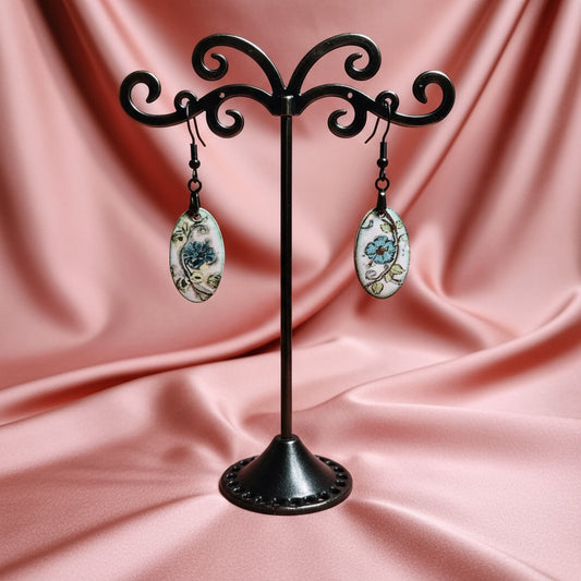 Bedrock Rose hand-painted oval enameled dangle earrings with blue blossoms and green leaves on white.