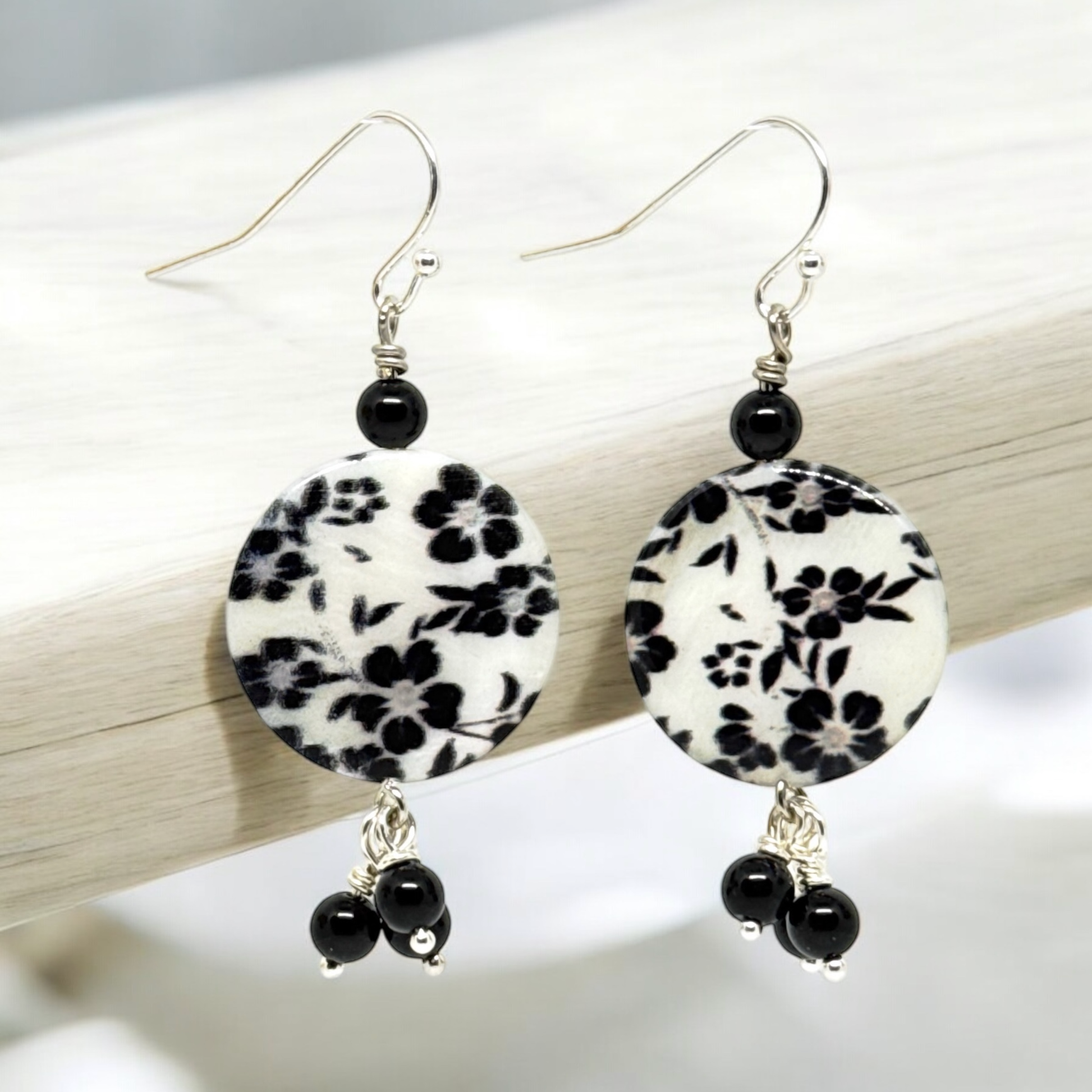 Close-up view of black and white floral drop earrings featuring porcelain discs with a delicate flower design and dark beads, showcasing their elegant and classic style.