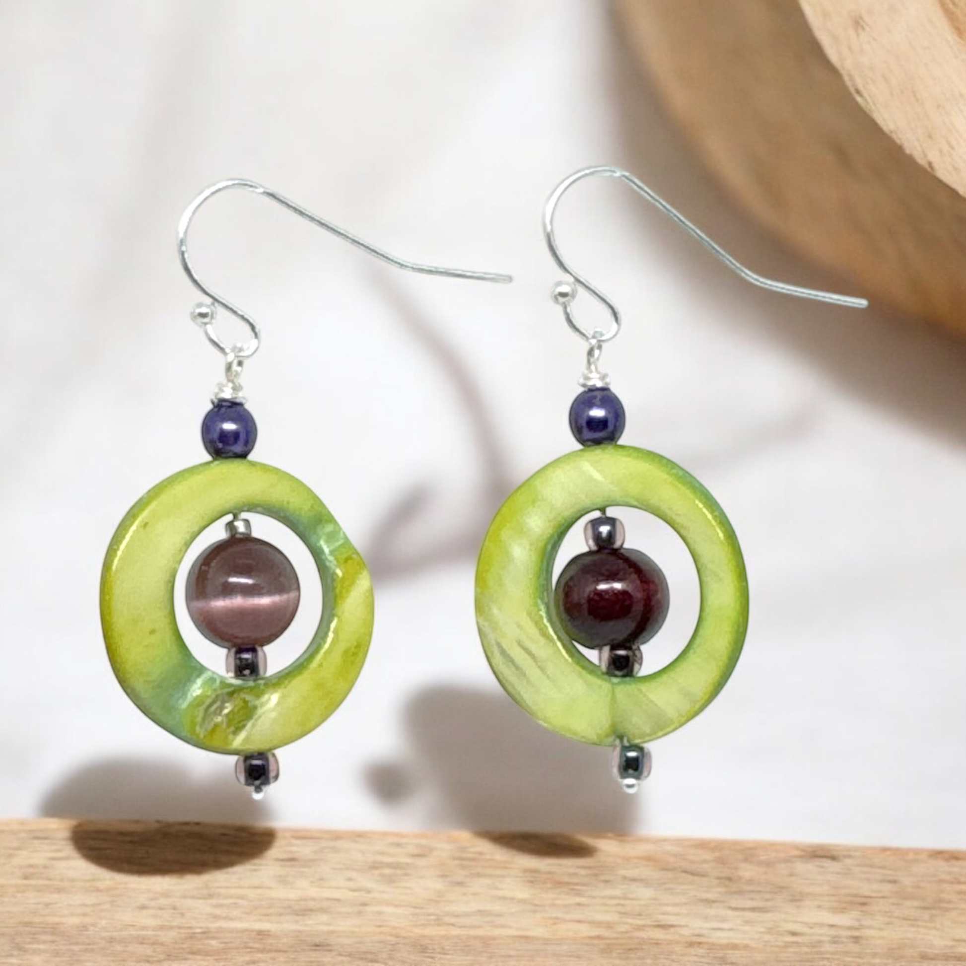 Close-up view of green shell and amethyst dangle earrings featuring circular shell pieces with natural variations and a purple amethyst bead in the center, showcasing their unique design.