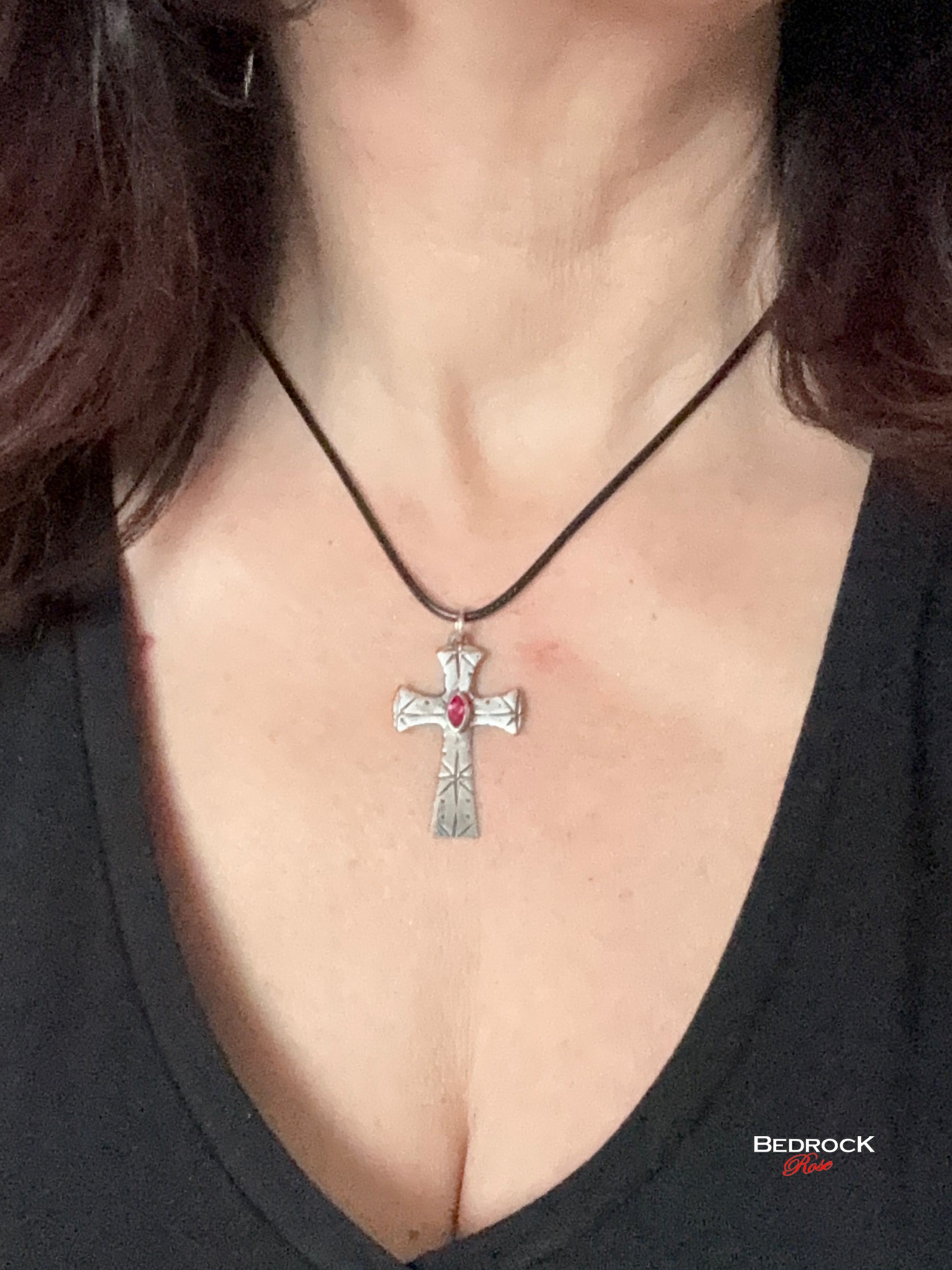 Front view of fine silver cross pendant with intricate pattern and ruby red marquise stone, Handmade necklace on model