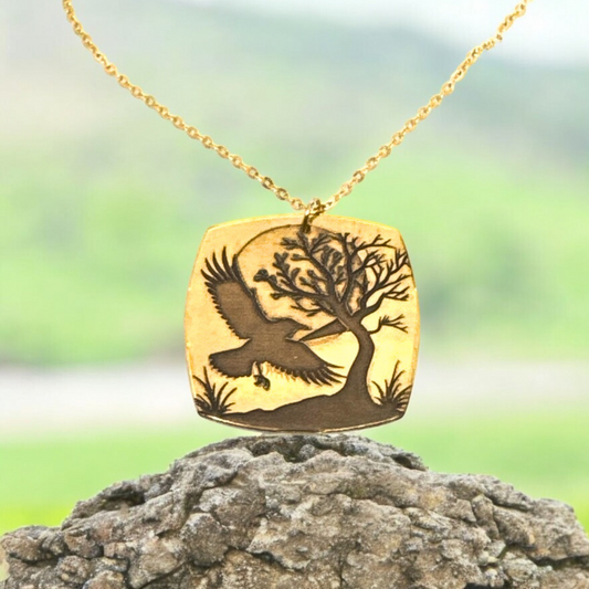 Detailed view of the laser-engraved crow and tree design on the gold-plated brass pendant, highlighting the intricate details.