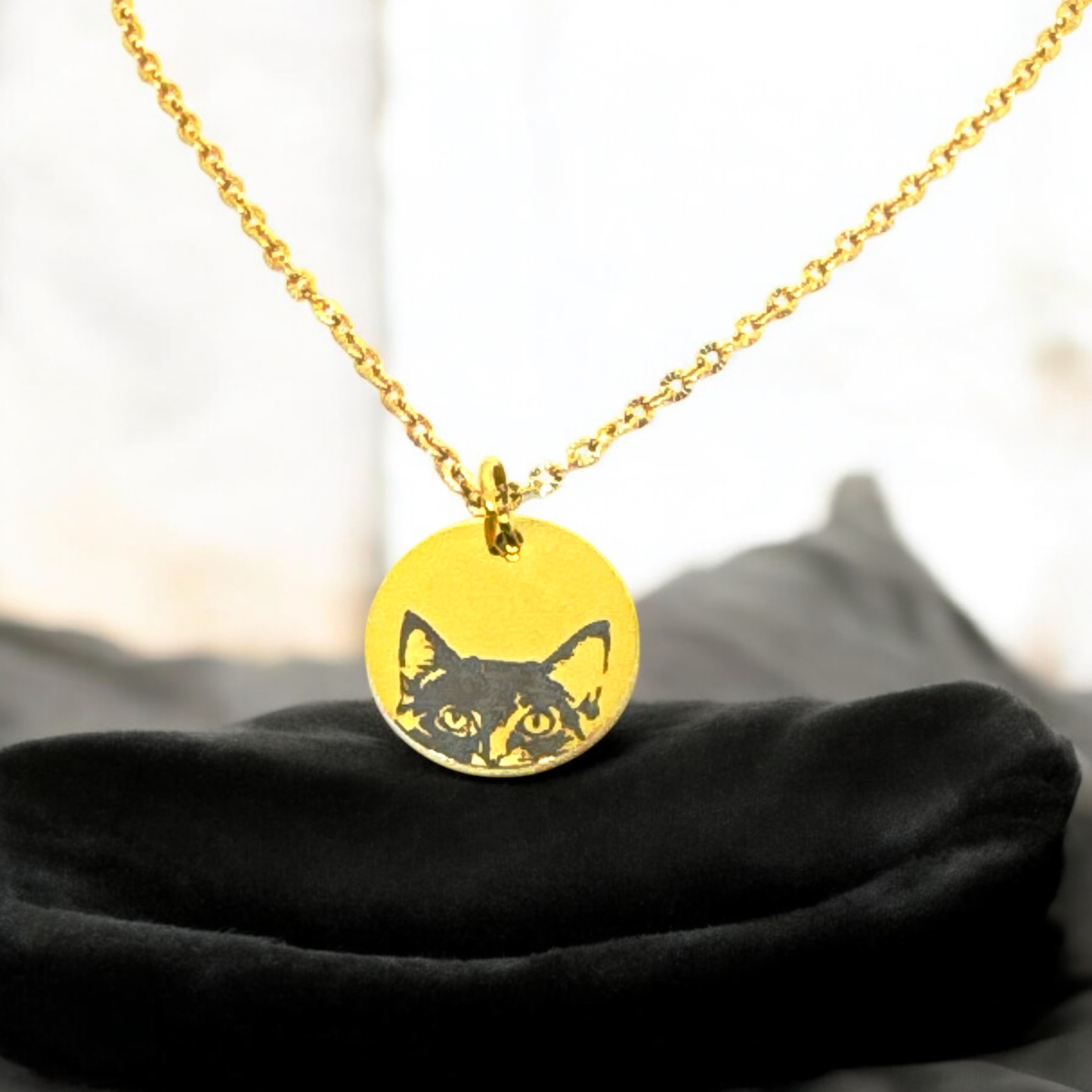 Close-up of a gold stainless steel necklace featuring a cat face design laser engraved on a round pendant, showing the cat peeking over the edge