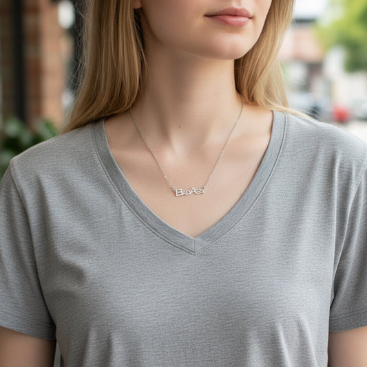 Bedrock Rose silver "Bad Ass" block letter pendant necklace on a stainless steel chain worn by a woman.
