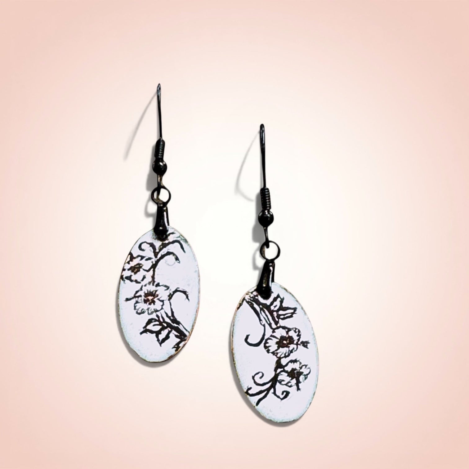 Bedrock Rose slender oval dangle earrings with black enamel floral design on white background.