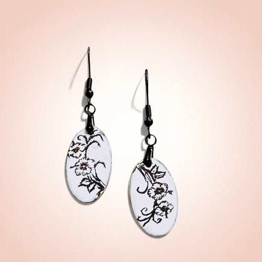 Bedrock Rose slender oval dangle earrings with black enamel floral design on white background.