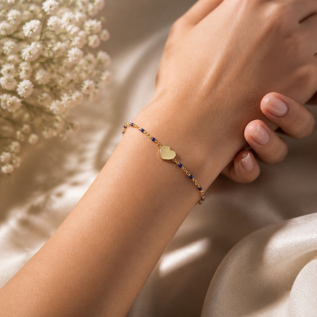 Bedrock Rose gold-tone cable chain bracelet with blue beads and a central heart charm worn on a woman's wrist.