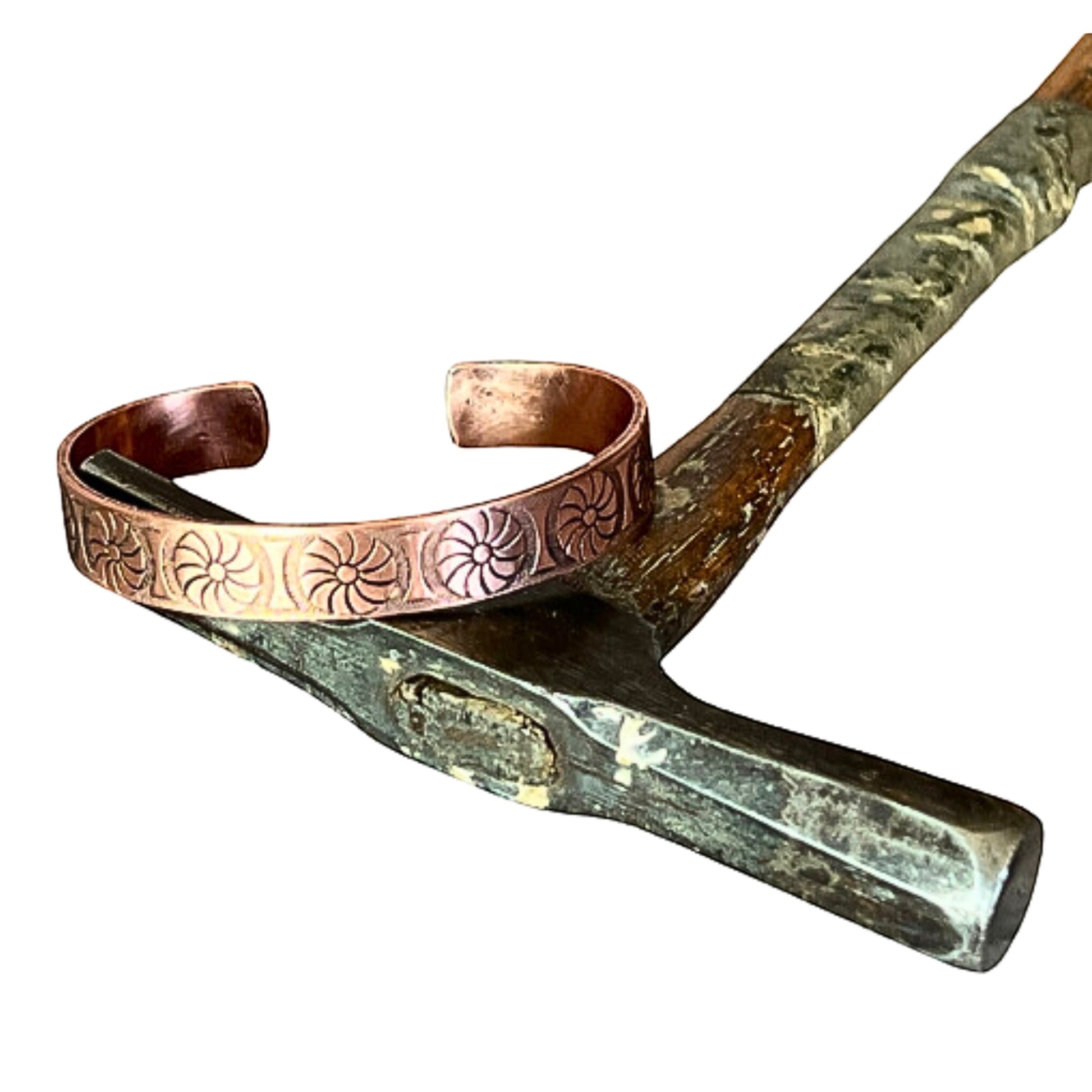 Bedrock Rose copper cuff bracelet with antique floral sunburst pattern resting on a vintage metal hammer