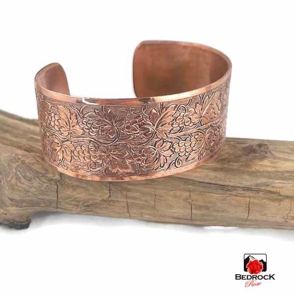 Bedrock Rose polished copper cuff bracelet featuring an intricate embossed grapevine pattern on a piece of driftwood.