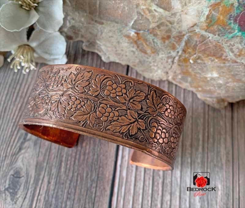Bedrock Rose copper cuff bracelet featuring an intricate polished grapevine pattern with detailed leaves and grapes.
