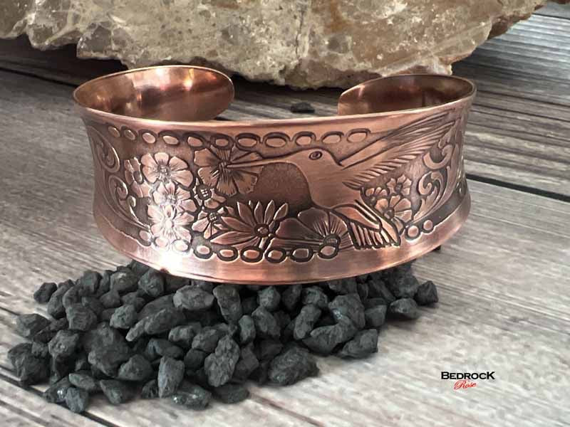 Bedrock Rose polished copper cuff bracelet featuring an intricate embossed hummingbird and floral design.