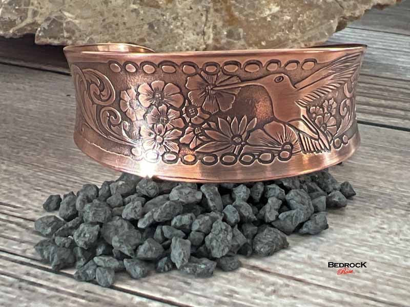 Bedrock Rose polished copper cuff bracelet featuring an embossed hummingbird and floral design on a rustic background.