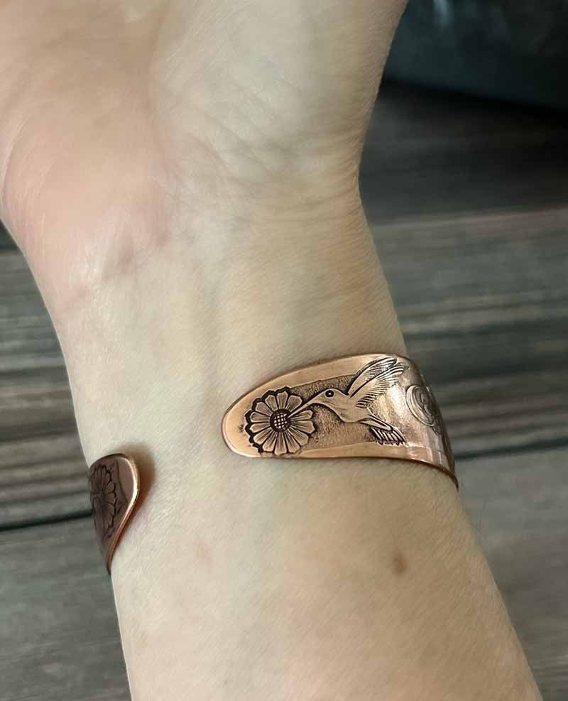Bedrock Rose copper cuff bracelet featuring an engraved hummingbird and flower design worn on a wrist