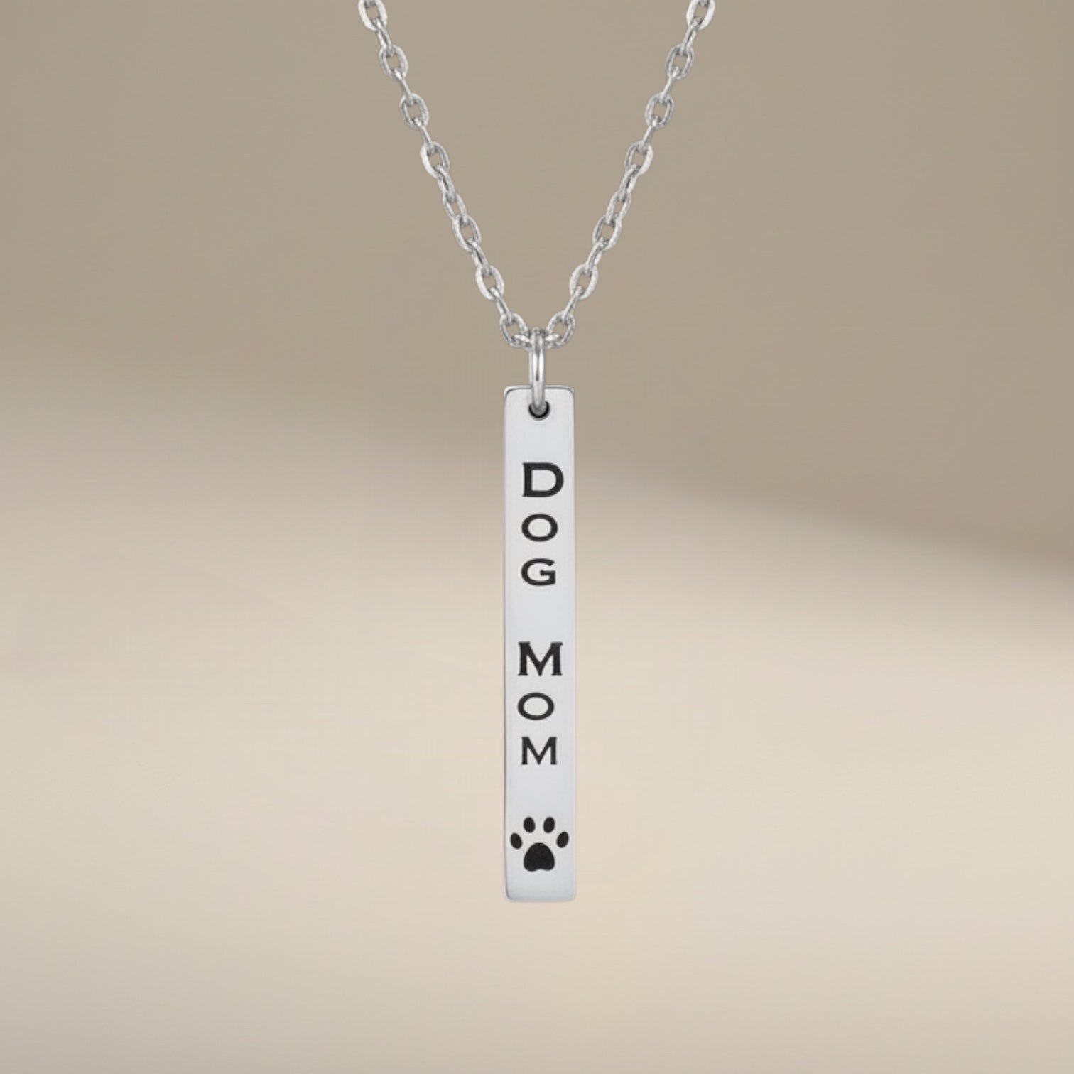 Bedrock Rose Dog Mom necklace with vertical bar pendant, engraved text and paw print detail, made of polished silver stainless steel.