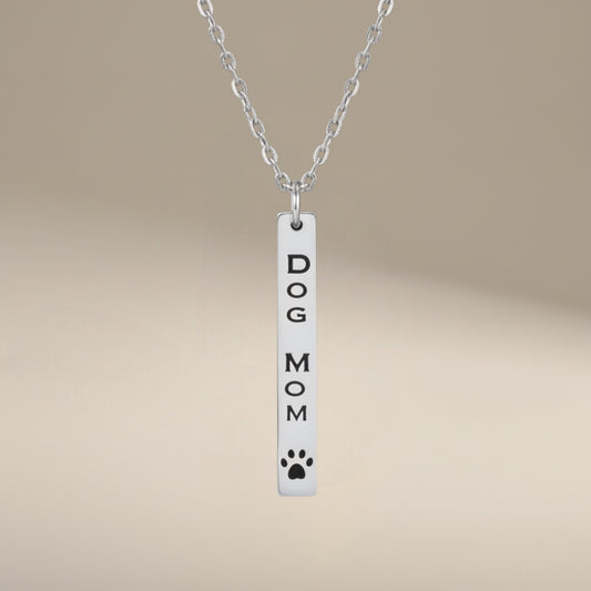 Bedrock Rose Dog Mom necklace with vertical bar pendant, engraved text and paw print detail, made of polished silver stainless steel.