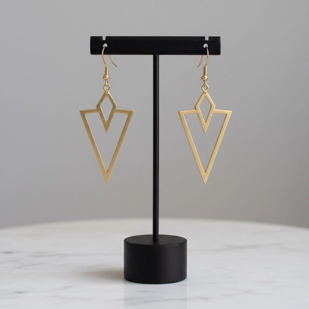 Bedrock Rose gold arrowhead dangling earrings with geometric laser-cut design on a black display stand.