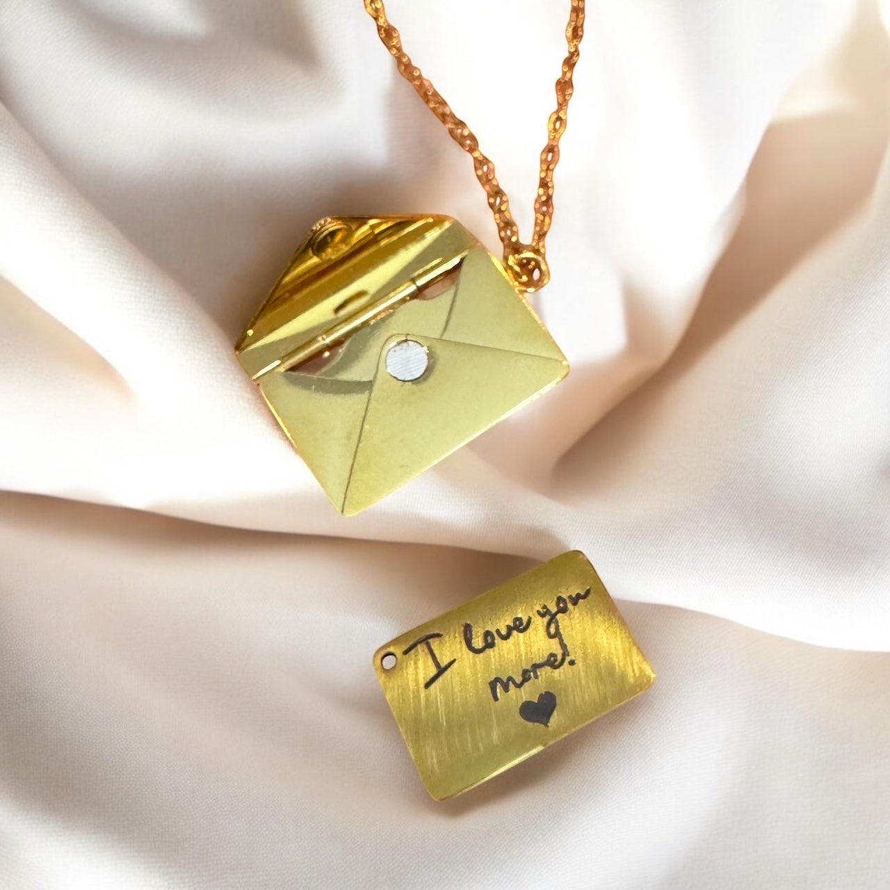 Bedrock Rose gold envelope necklace with a removable engraved letter insert on a soft white fabric background.