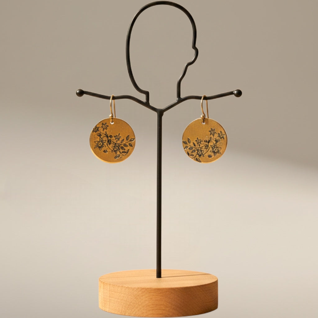 Bedrock Rose gold disc dangle earrings featuring delicate laser-engraved floral vine designs on a display stand.