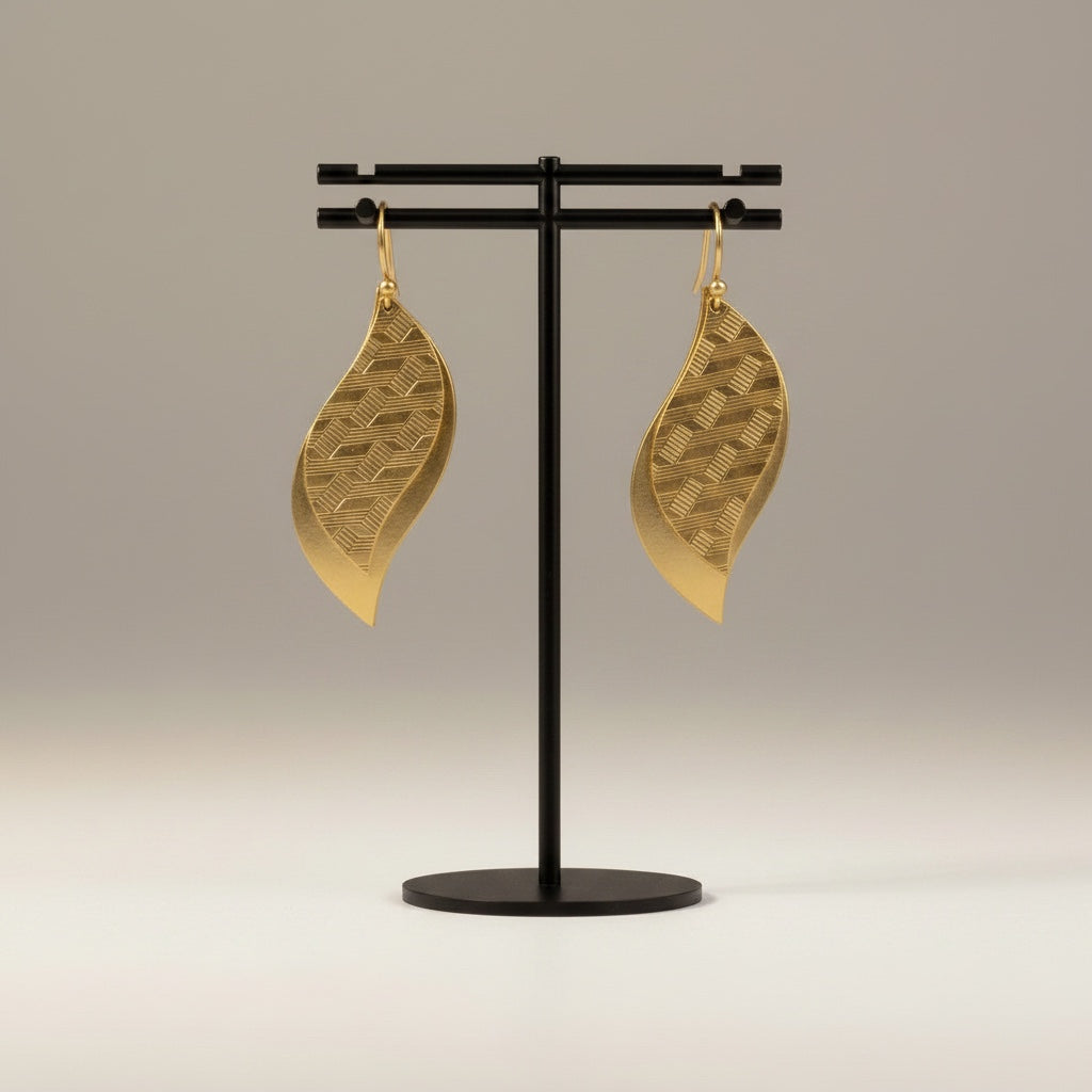 Bedrock Rose gold leaf dangle earrings with geometric etched brass patterns hanging on a black display stand.