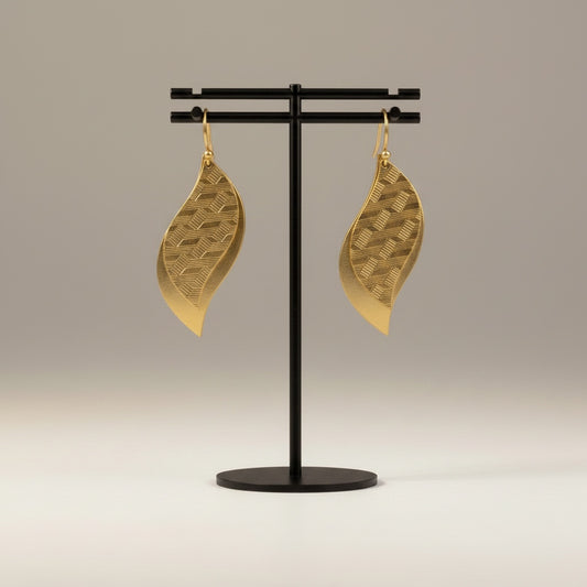 Bedrock Rose gold leaf dangle earrings with geometric etched brass patterns hanging on a black display stand.