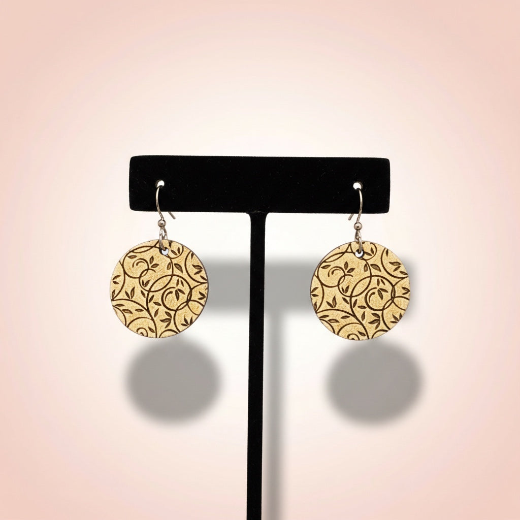Bedrock Rose golden disc earrings featuring an intricate laser-etched botanical vine lattice pattern on a display stand.