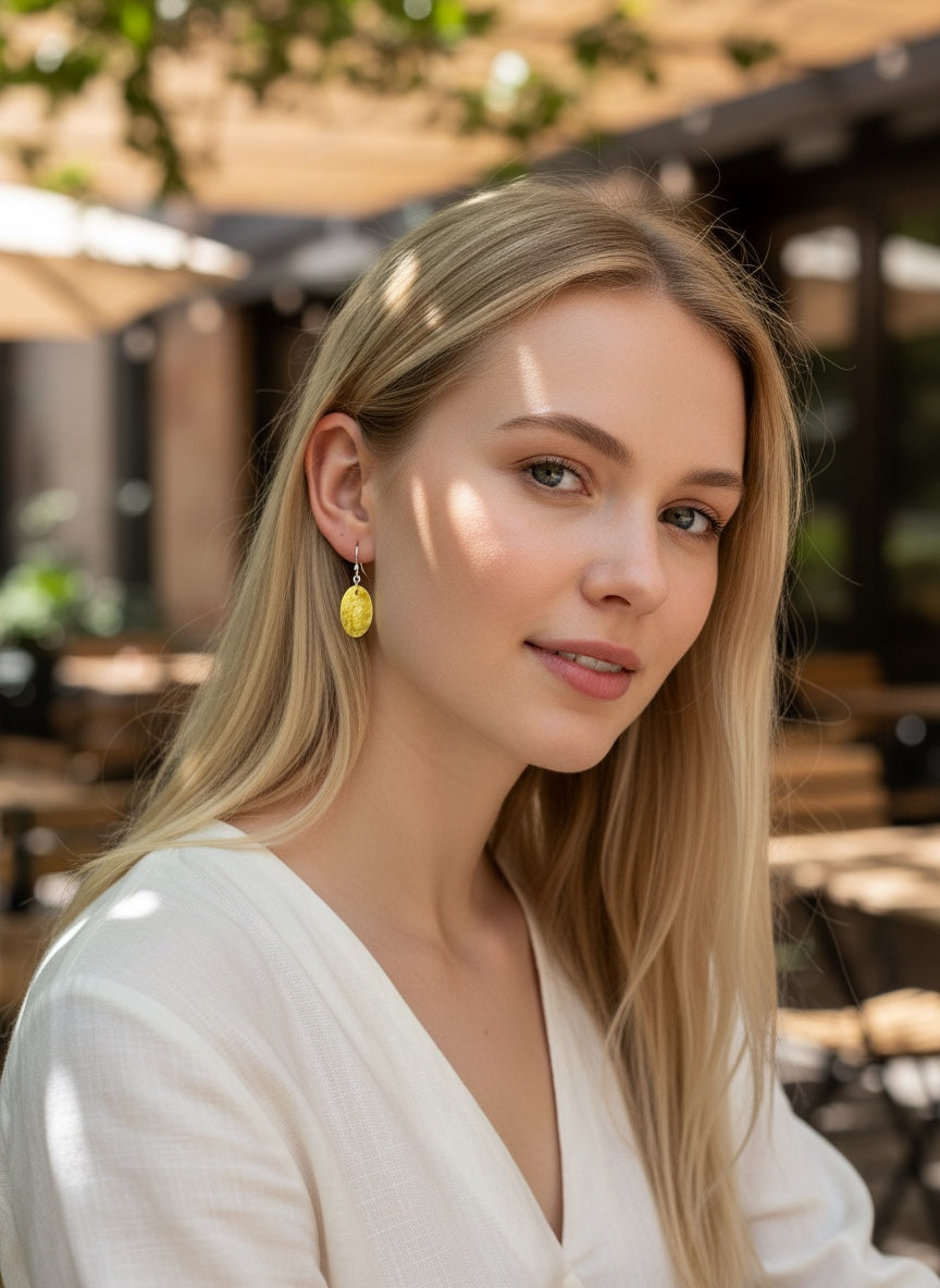 Bedrock Rose oval honeycomb earrings in amber-gold enamel on silver worn by a blonde woman in an outdoor cafe