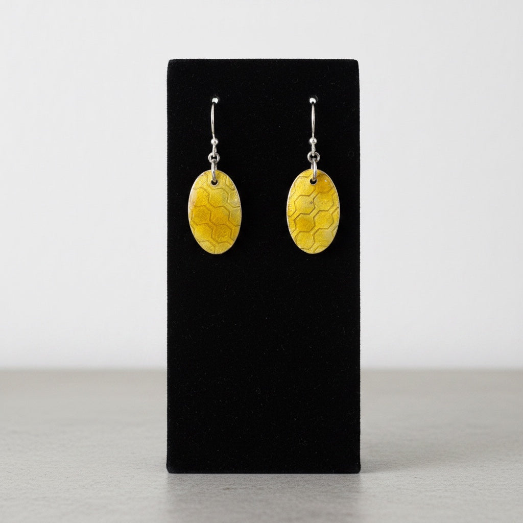 Bedrock Rose oval earrings featuring a golden honeycomb pattern in amber glass enamel over textured fine silver.