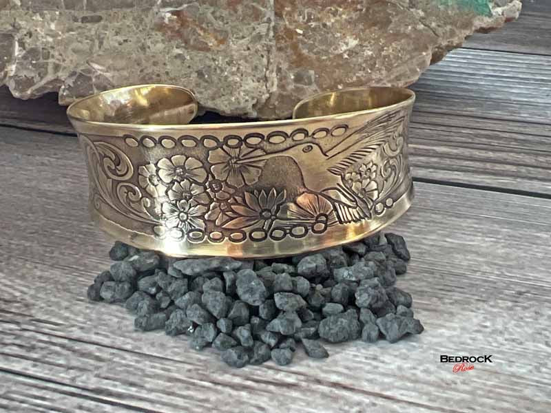 Bedrock Rose polished brass cuff bracelet featuring an intricate embossed hummingbird and floral design.