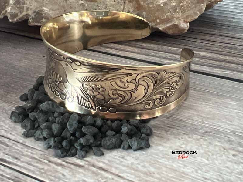 Bedrock Rose polished brass hummingbird cuff bracelet with intricate floral engraving and an open slip-on design.