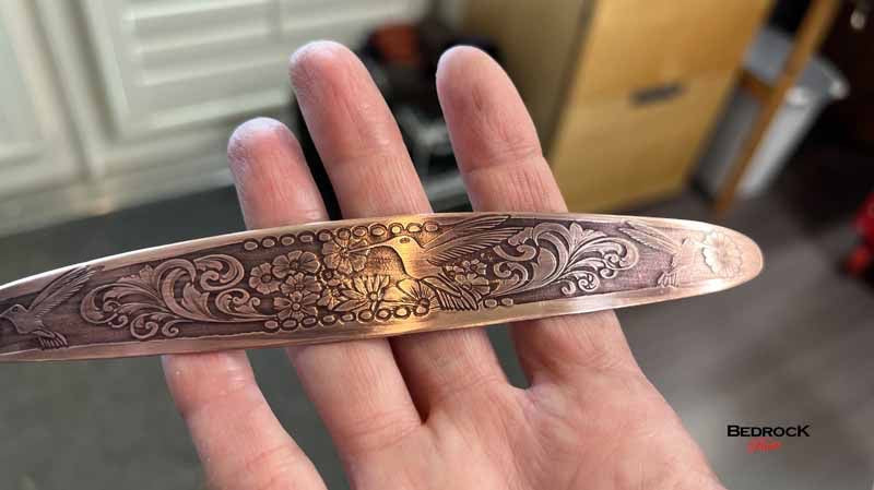 Bedrock Rose polished copper cuff bracelet featuring an intricate embossed hummingbird and floral design.