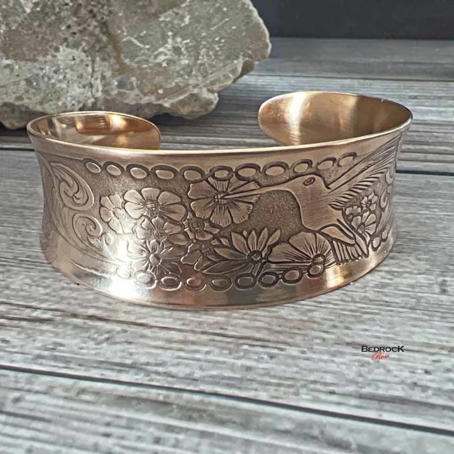 Bedrock Rose polished copper cuff bracelet featuring an intricate embossed hummingbird and floral design.