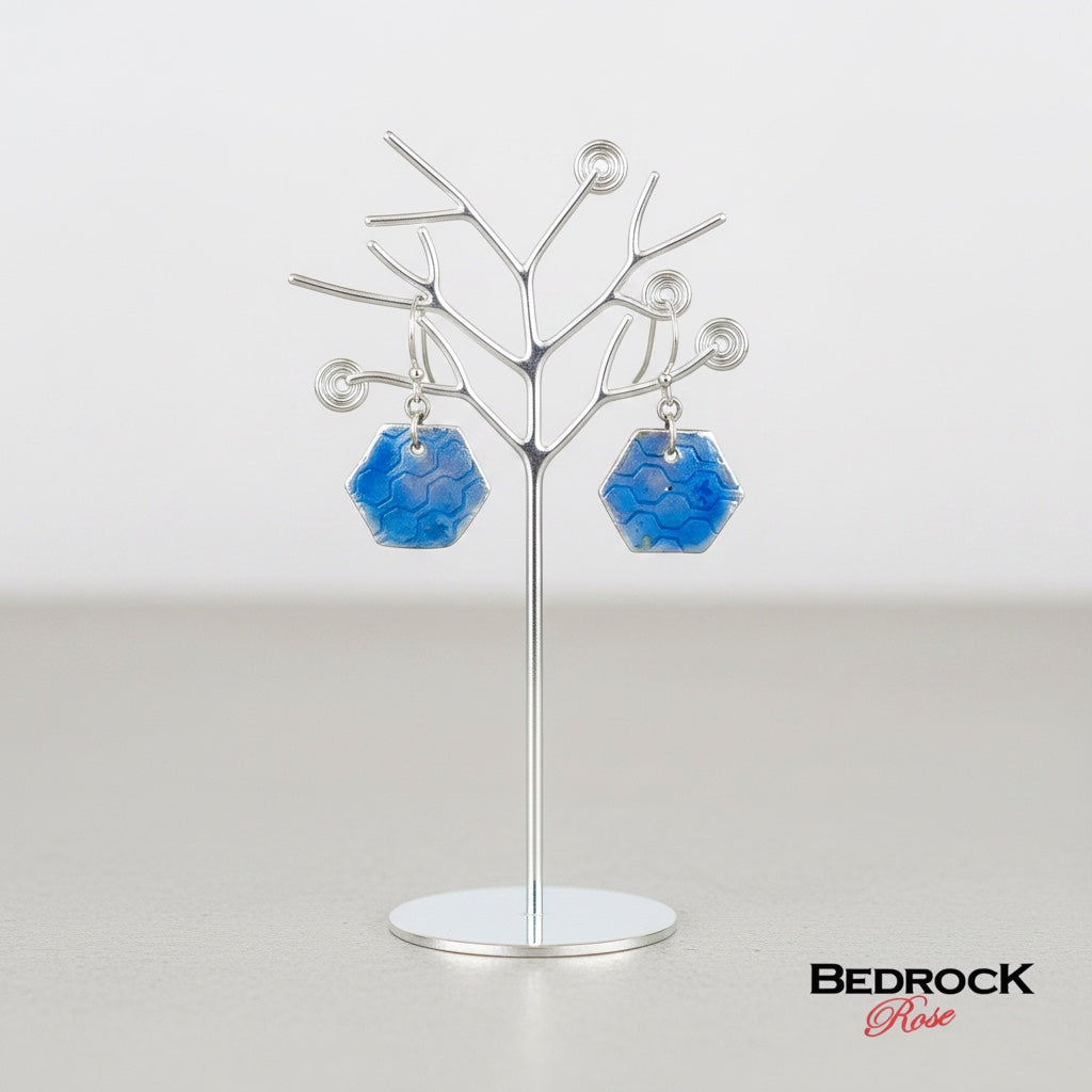 Bedrock Rose periwinkle blue enamel hexagon earrings with honeycomb texture on fine silver hanging on a display stand.