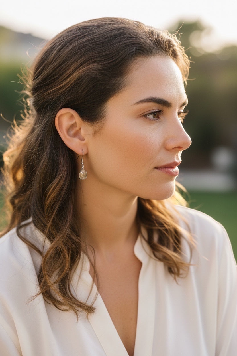 Bedrock Rose prong set pear rutilated quartz drop earrings on a woman with wavy brown hair.