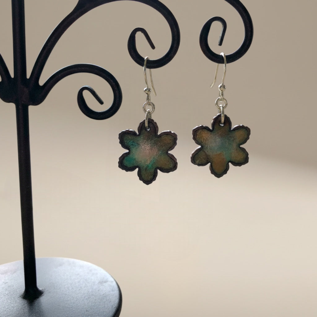 Bedrock Rose serrated flower dangle earrings in moss green enamel and dark copper hanging on a black display stand.