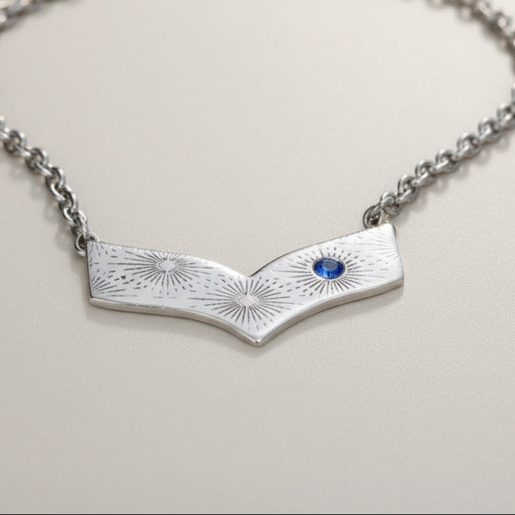 Bedrock Rose silver chevron pendant necklace with blue gemstone accent and sunburst engraving.