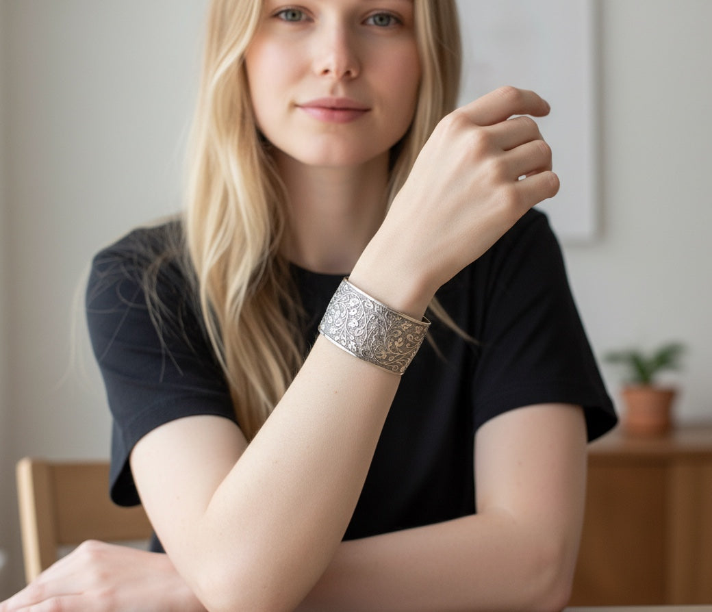 Bedrock Rose silver wide cuff bracelet featuring an intricate leafy vine pattern worn by a woman in a black shirt.