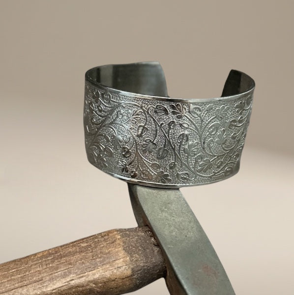 Bedrock Rose silver wide cuff bracelet featuring an intricate embossed leafy vine pattern on a polished metal surface.