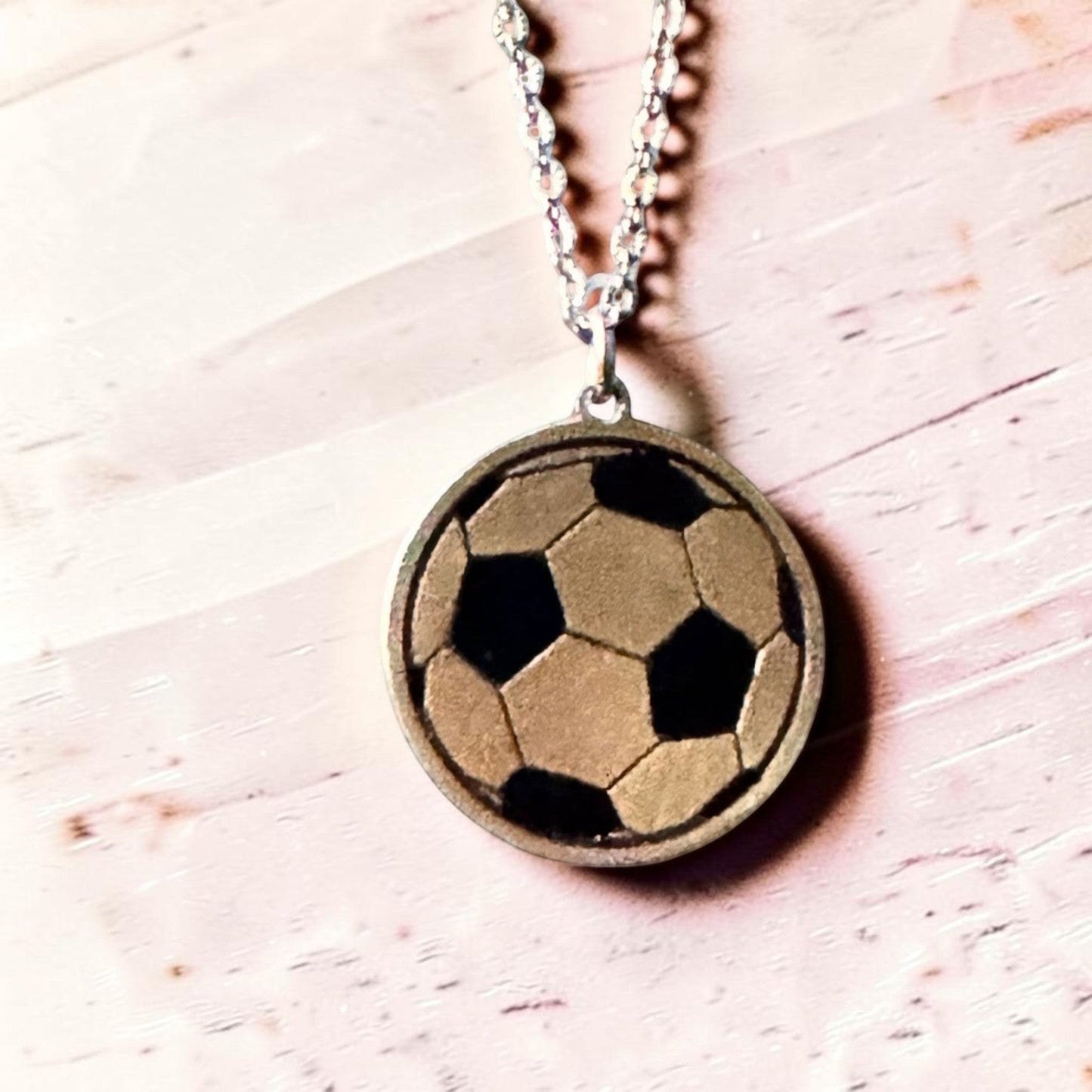 Bedrock Rose laser-engraved brass soccer ball pendant necklace on a stainless steel chain against a light background.
