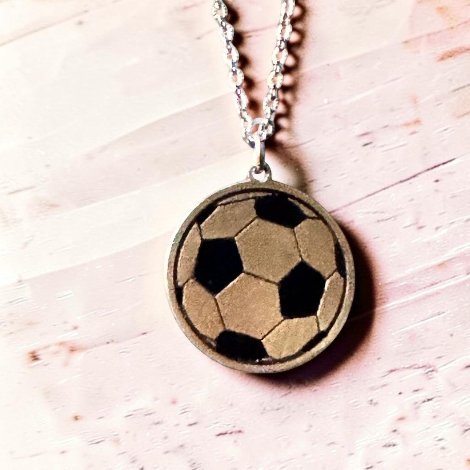 Bedrock Rose laser-engraved brass soccer ball pendant necklace on a stainless steel chain against a light background.