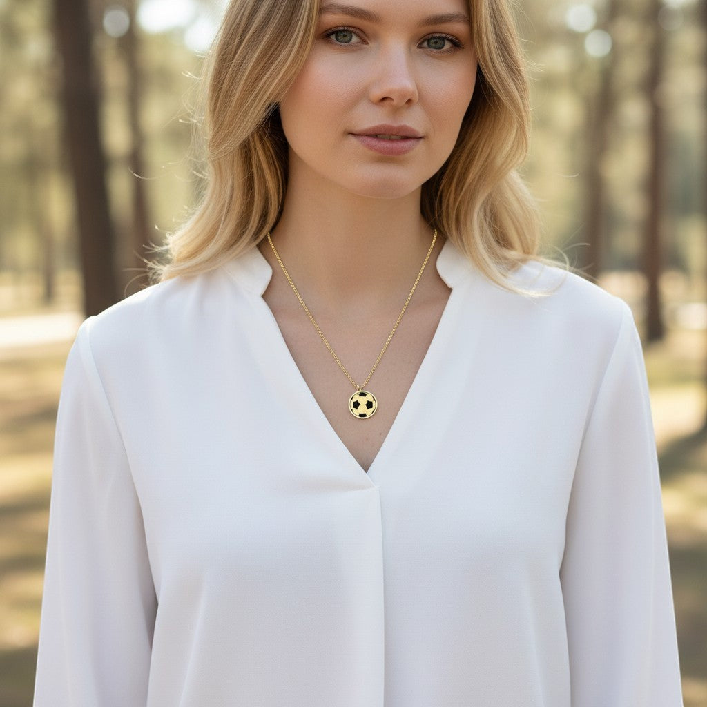 Bedrock Rose brass soccer ball pendant necklace on a woman wearing a white blouse in a natural outdoor setting.