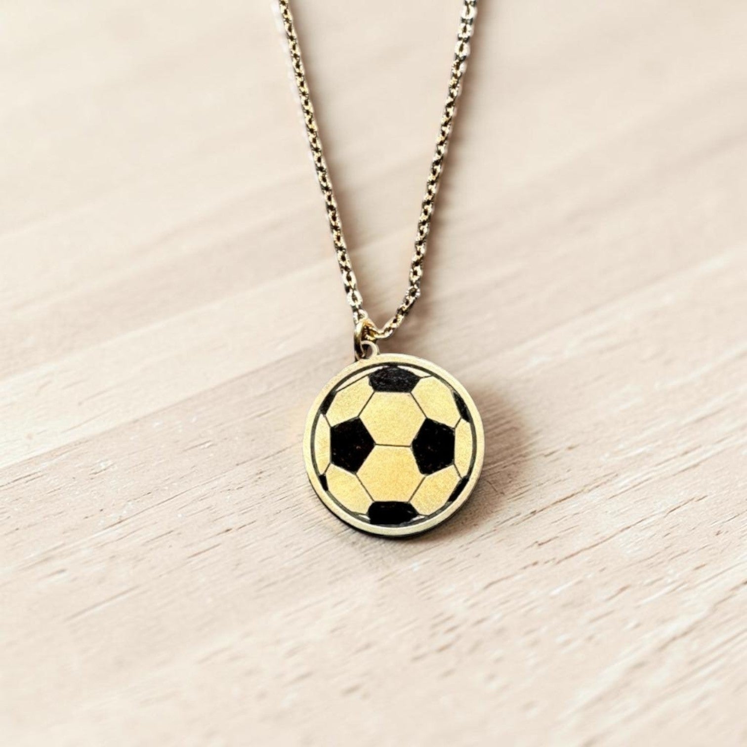 Bedrock Rose laser-engraved brass soccer ball pendant necklace on a stainless steel chain.