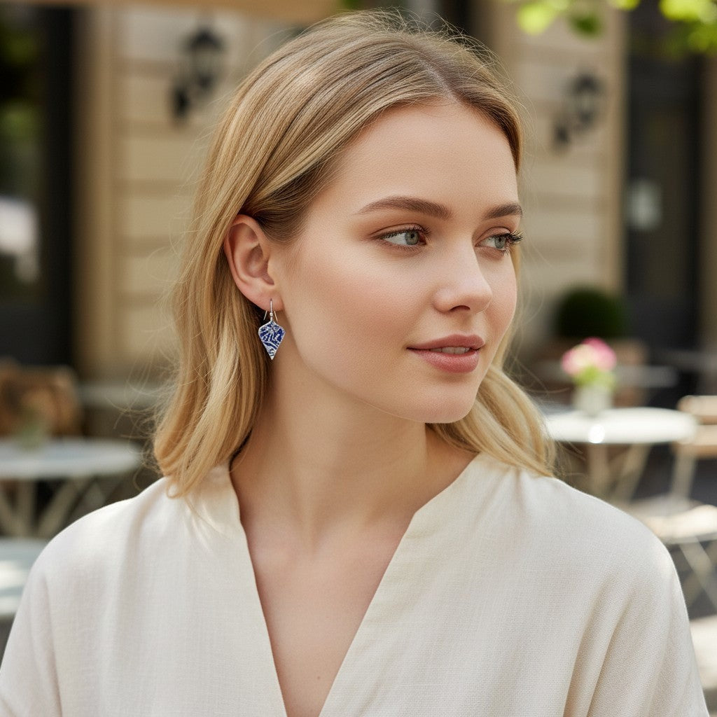 Model wearing Bedrock Rose sterling silver shield earrings with blue abstract branch texture and patina finish.