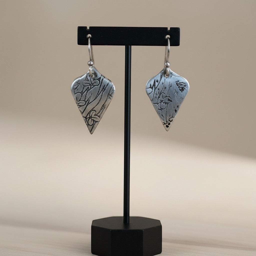 Bedrock Rose sterling silver shield dangle earrings with oxidized botanical texture and floral details on display.