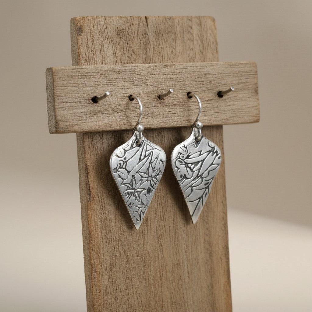 Bedrock Rose sterling silver shield-shaped dangle earrings with oxidized floral vine texture on a wooden display.