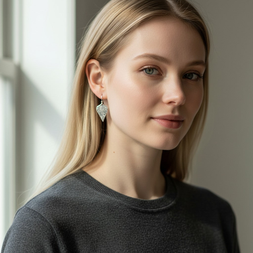 Model wearing Bedrock Rose sterling silver shield dangle earrings with an oxidized floral vine texture.