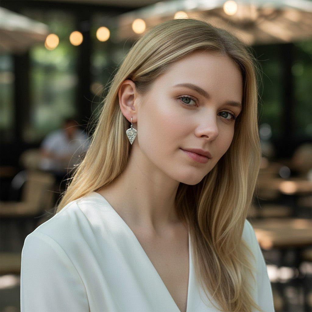 Bedrock Rose sterling silver shield dangle earrings with lotus texture and oxidized patina worn by a blonde woman.