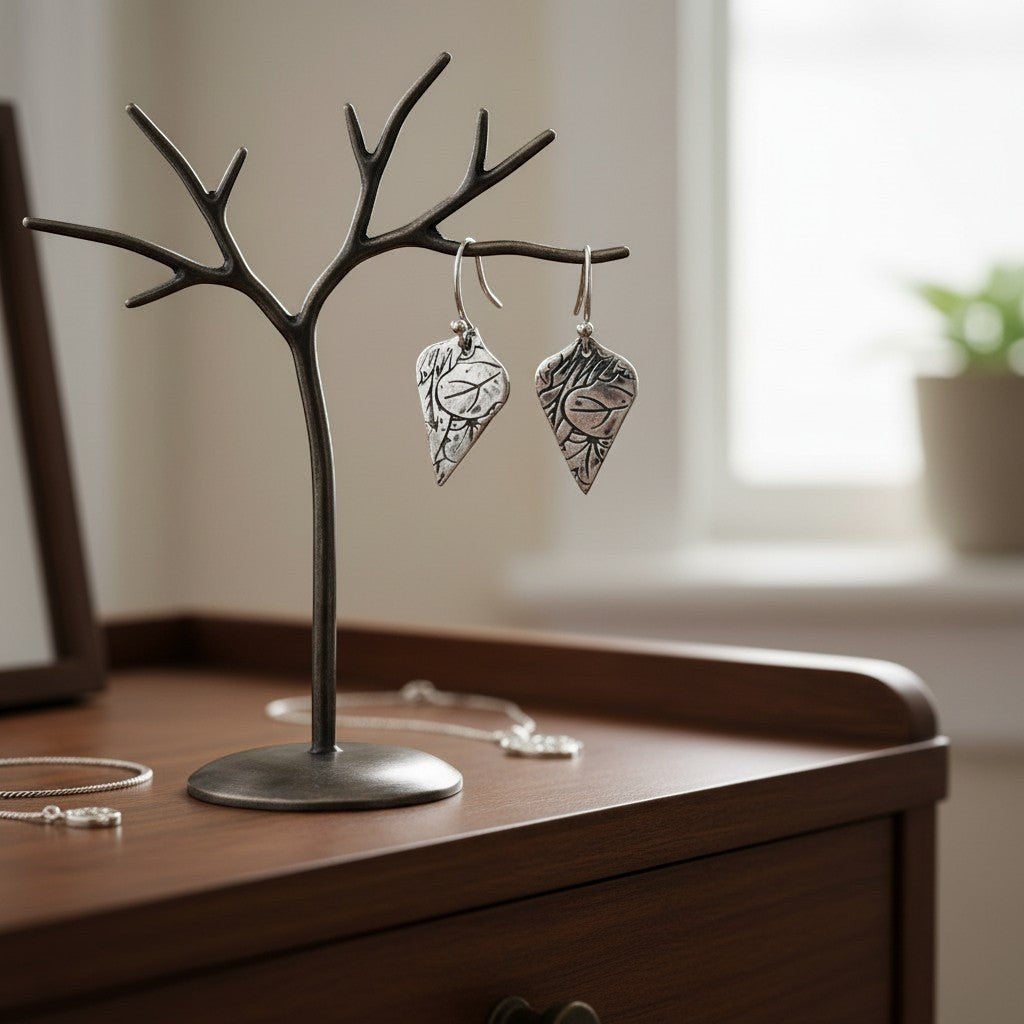 Bedrock Rose sterling silver shield-shaped dangle earrings with oxidized lotus texture on a metal tree display stand.