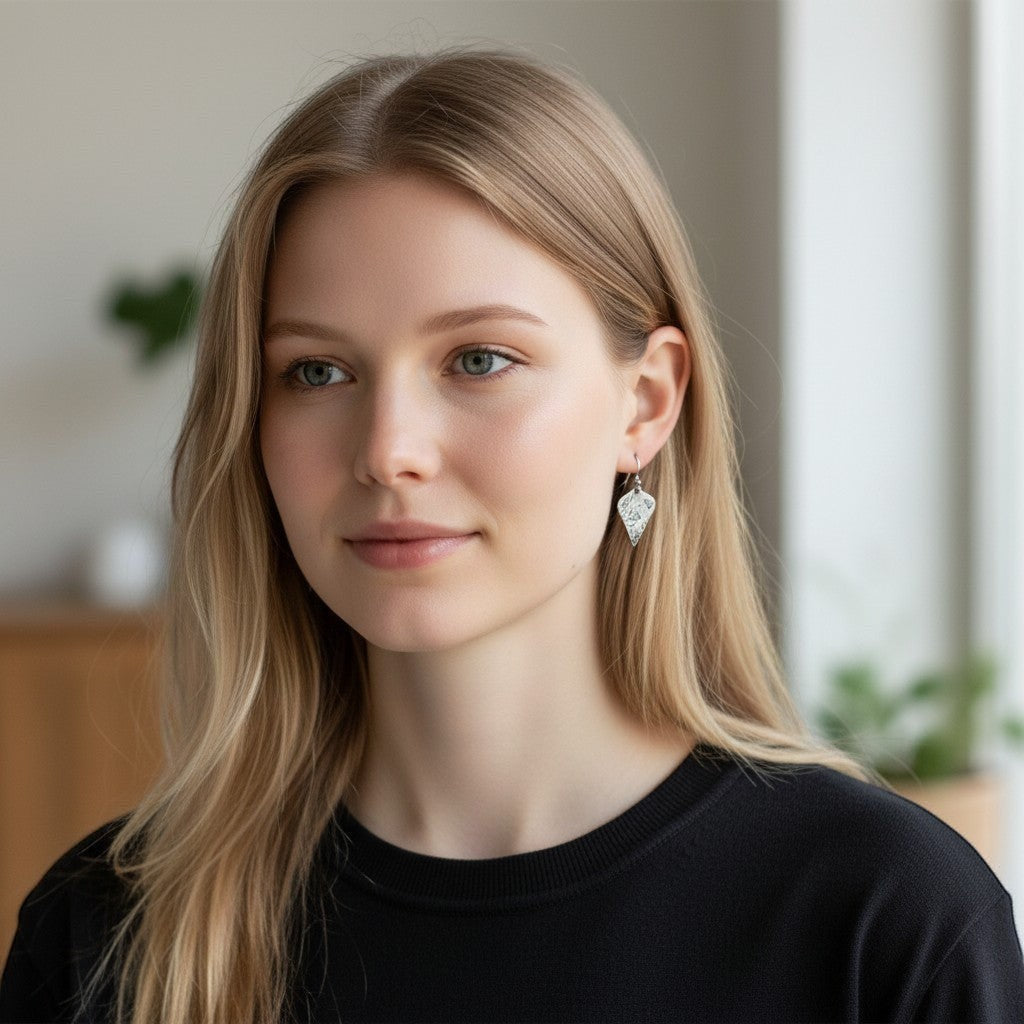 Model wearing Bedrock Rose sterling silver shield dangle earrings with oxidized botanical texture and floral details.