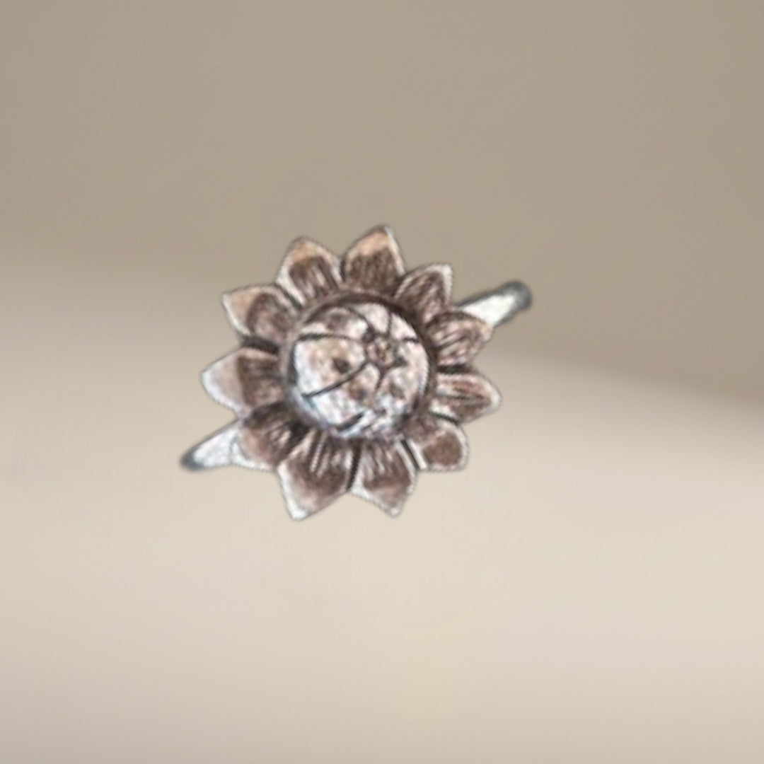 Bedrock Rose sterling silver sunflower ring with antiqued patina on a hand, surrounded by purple and white flowers.